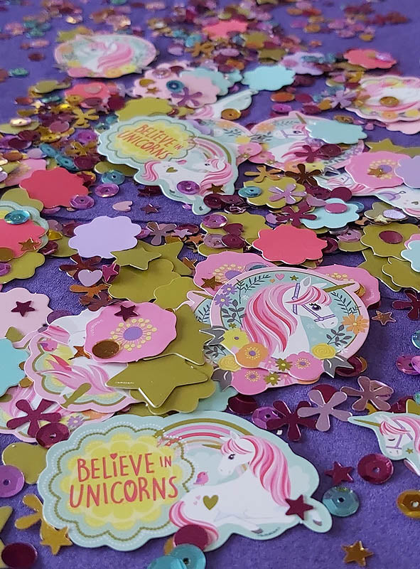 Die Tischdekoration „Einhorn-Konfetti-Mix“ besteht aus farbenfrohem Konfetti mit Einhorn-Motiven, Blumen, Sternen und Pailletten, die wunderschön auf einem violetten Hintergrund verteilt sind und so für eine zauberhafte Partydekoration sorgen. Einige Elemente sind mit dem Schriftzug „BELIEVE IN UNICORNS“ verziert und zeigen illustrierte Einhörner mit rosa Mähnen, wodurch sich dieser Mix perfekt für eine bezaubernde Tischdekoration bei jeder Feier eignet.