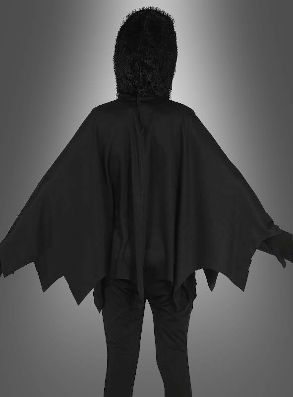 Eine Person in einem schwarzen Spinnen-Poncho für Kinder mit einem gezackten Umhang und einer pelzigen Kapuze, die mit dem Rücken zur Kamera vor einem grauen Hintergrund mit Farbverlauf steht – perfekt als Halloween-Kinderkostüm oder leuchtendes Spinnenkostüm für fantasievolles Spielen.
