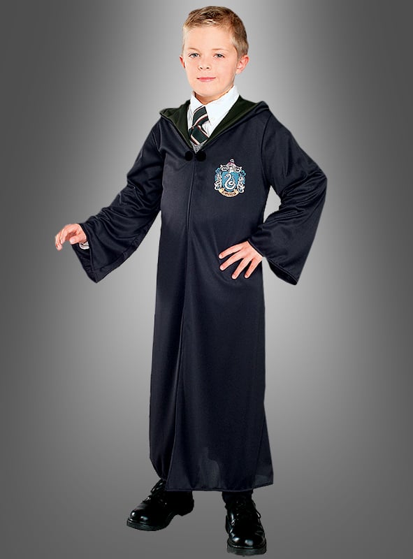Ein Kind, das eine Slytherin-Schuluniform trägt – darunter die Slytherin-Robe von Draco Malfoy aus „Harry Potter“, ein weißes Hemd, eine gestreifte Krawatte und schwarze Schuhe –, steht vor einem schlichten grauen Hintergrund.
