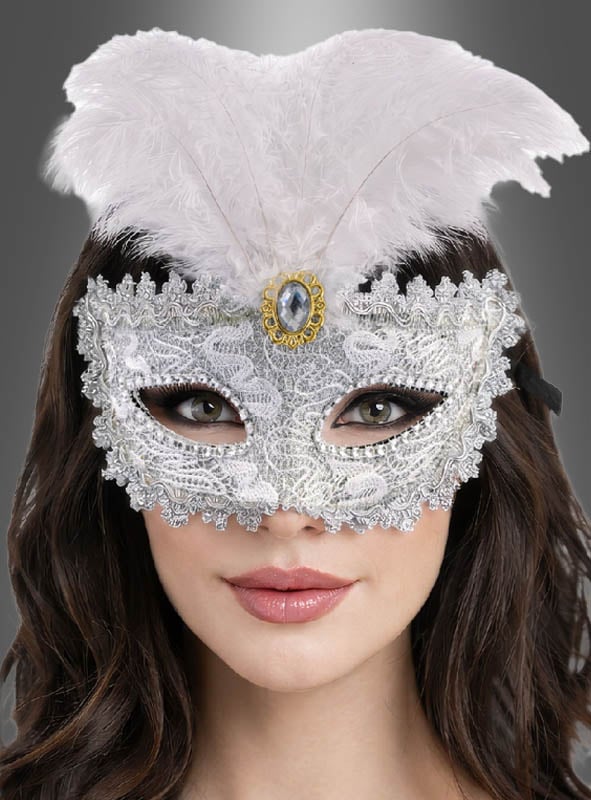 Eine Person, die die „Maskenball-Augenmaske mit Spitze, silber“ trägt, verziert mit weißen Federn und einem Zierstein, vor einem grauen Hintergrund mit Farbverlauf.