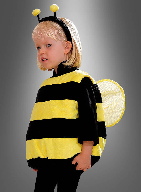Ein kleines Kind, das ein schwarzes und gelbes „Plüsch-Bienenkostüm für Kinder Deluxe“ mit Flügeln und Fühlern trägt und vor einem grauen Hintergrund steht.