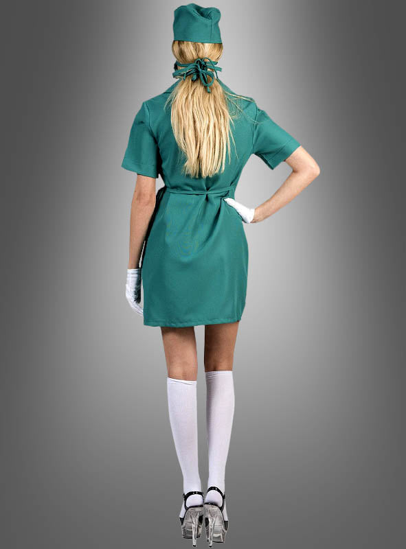 Eine Person in einem kurzen grünen OP-Schwester-Kostüm (Wickelkleid), weißen Handschuhen, weißen Kniestrümpfen und durchsichtigen High Heels steht mit dem Rücken zur Kamera vor einem grauen Hintergrund.