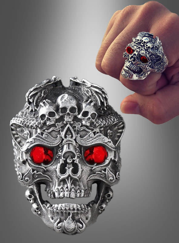 Ein verstellbarer Totenkopf-Ring aus Silber mit filigranen Verzierungen und roten Edelsteinaugen wird sowohl an einer Hand als auch in einer Nahaufnahme vor grauem Hintergrund gezeigt – ideal als auffälliger Halloween-Schmuck.