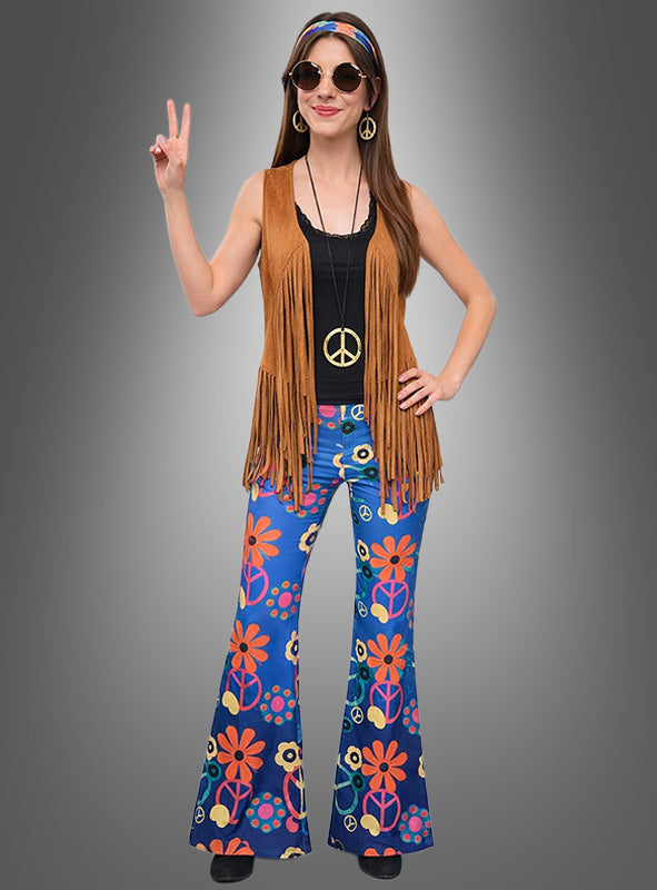 Eine Frau, die das Hippie-Kostüm-Set „Blue Peace“ trägt – bestehend aus einer von den 1970er Jahren inspirierten Fransenweste, einer Halskette mit Peace-Zeichen, einer geblümten Schlaghose und einer Sonnenbrille –, posiert mit einer Peace-Zeichen-Geste vor einem grauen Hintergrund.