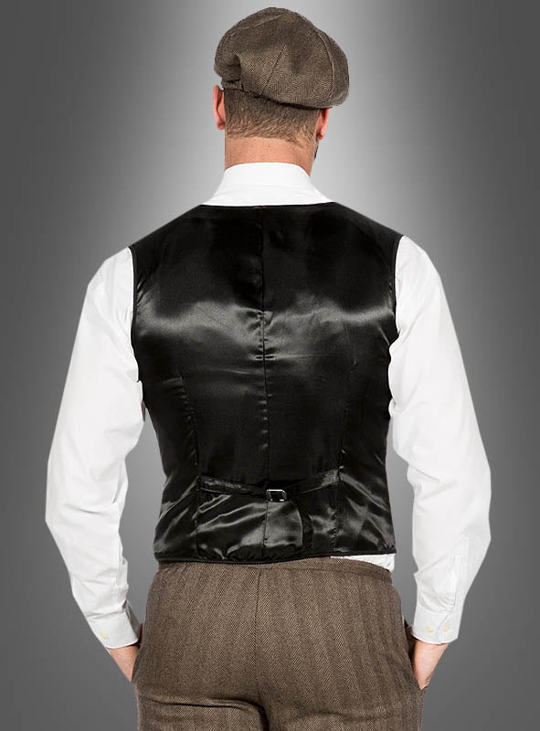 Ein Mann, der das „20er-Jahre-Modekostüm John“ trägt – bestehend aus einer schwarzen Satinweste, einem weißen Hemd, einer braunen Hose und einer Schirmmütze –, steht mit dem Rücken zur Kamera vor einem grauen Hintergrund mit Farbverlauf und verkörpert damit den klassischen „Peaky Blinders“-Stil sowie die zeitlose Mode der 1920er Jahre.