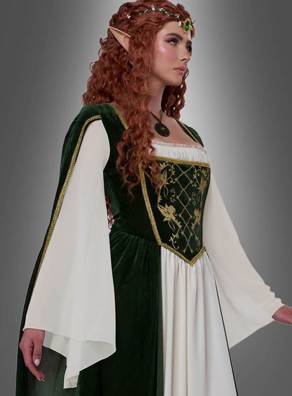 Eine Frau in einem grün-weißen, mittelalterlich anmutenden Kleid mit langen Ärmeln – einem exquisiten „Elfenkönigin Emerald“-Damenkostüm – trägt eine Halskette, einen mit Edelsteinen besetzten Kopfschmuck und spitze Elfenohren, während sie vor einem grauen Hintergrund mit Farbverlauf steht. Dieses elegante Fantasy-Kostüm eignet sich perfekt, um sich in eine Elfenkönigin zu verwandeln.