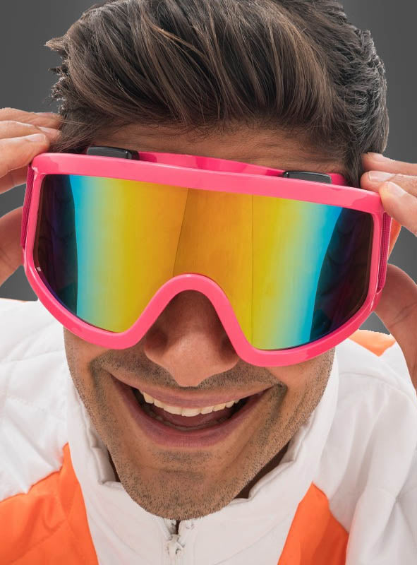 Eine Person in einer weiß-orangefarbenen Jacke lächelt, während sie eine große, pinkfarbene, reflektierende Skibrille „Karneval Neon“ zurechtzieht – ein auffälliges Après-Ski-Accessoire, das sich perfekt für festlichen Winterspaß eignet.