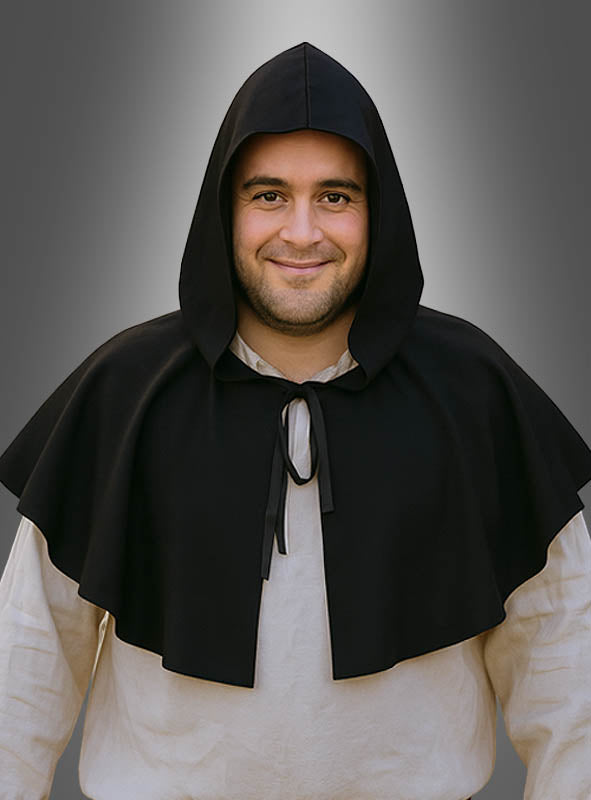Eine Person, die einen schwarzen „Mittelalter-Schulterumhang mit Kapuze“ über einem weißen Hemd trägt, steht vor einem grauen Hintergrund mit Farbverlauf und lächelt in die Kamera – ein perfekter Look für jeden Liebhaber mittelalterlicher Kostüme.
