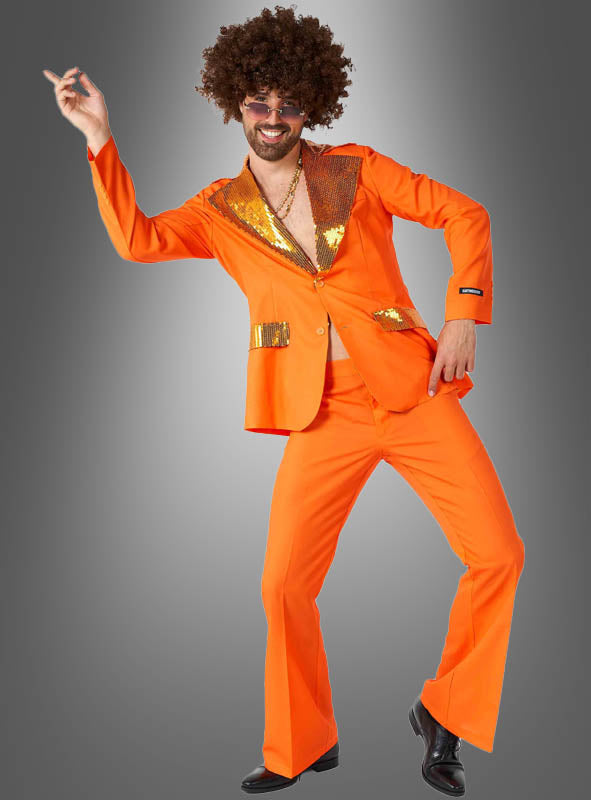 Ein Mann, der den „Orangener Disco-Anzug“ trägt und eine Afro-Perücke auf dem Kopf hat, nimmt vor einem grauen Hintergrund mit Farbverlauf eine Tanzpose ein und verkörpert damit das lebhafte Flair eines klassischen 70er-Jahre-Kostüms.
