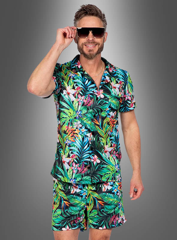 Ein Mann mit Sonnenbrille und einem farbenfrohen „Tropisches Hawaii“-Set aus Hemd und Shorts steht vor einem grauen Hintergrund und lächelt in die Kamera – und präsentiert damit das perfekte Sommeroutfit.