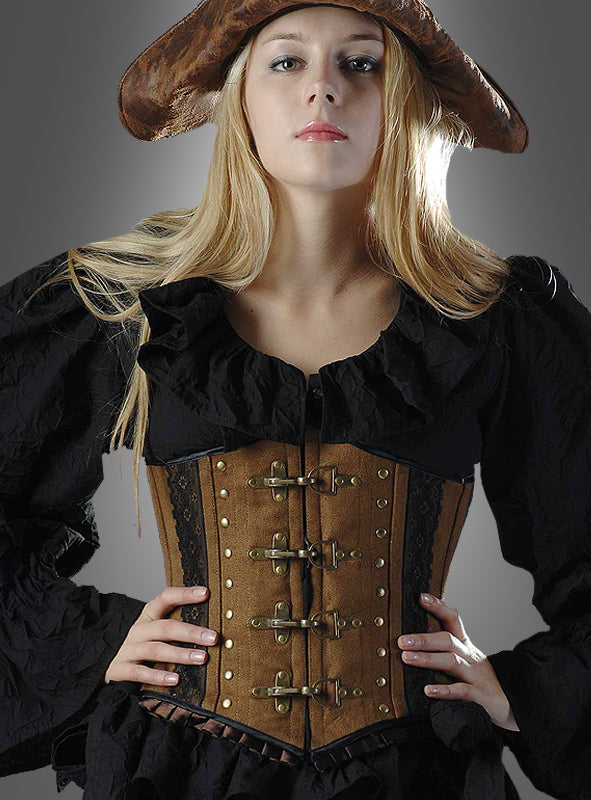 Eine Frau mit einem braunen Piratenhut, einer schwarzen Rüschenbluse und dem „Antiklook Korsage braun Steampunk“-BH mit Metallschnallen und Wildlederoptik, die mit den Händen in den Hüften vor einem grauen Hintergrund posiert.