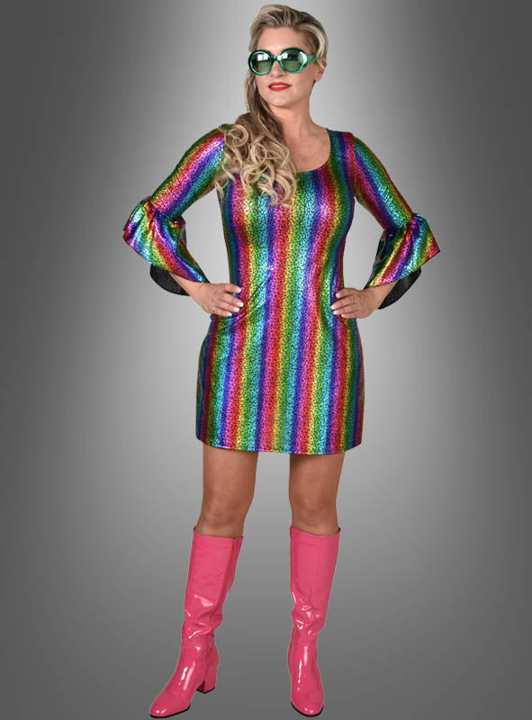 Eine Frau, die das „Hologramm Partykleid Regenbogen“ trägt – ein glänzendes Kleid mit Regenbogenstreifen –, dazu eine große Sonnenbrille und rosa kniehohe Stiefel, steht vor einem grauen Hintergrund und erinnert an den ikonischen Stil der Disco-Mode der 70er Jahre.
