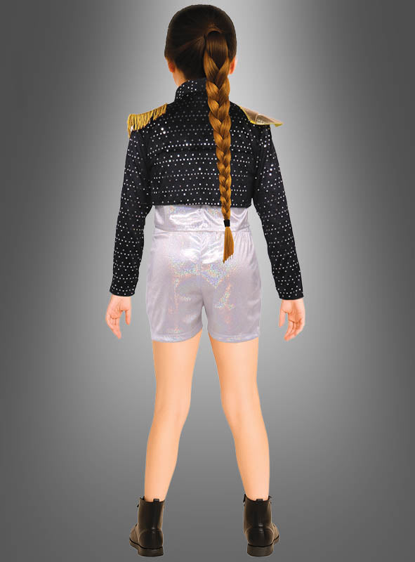 Ein Kind mit einem langen Zopf steht mit dem Rücken zur Kamera und trägt das „K-Pop Star Sängerin“-Kinderkostüm, bestehend aus einer schwarzen Paillettenjacke mit goldenen Akzenten an den Schultern, glänzenden silbernen Shorts und schwarzen Stiefeln vor einem grauen Hintergrund mit Farbverlauf.