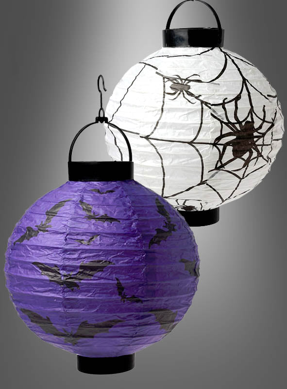 Zwei runde Laternen aus dem LED-Halloween-Set „Papierlaterne Fledermaus oder Spinnen“ – eine weiße, verziert mit schwarzen Spinnen- und Spinnennetzmotiven, und eine violette mit schwarzen Fledermaus-Silhouetten – hängen nebeneinander vor einem grauen Hintergrund und sind damit ein echter Blickfang als Halloween-Dekoration für jede gruselige Feier.