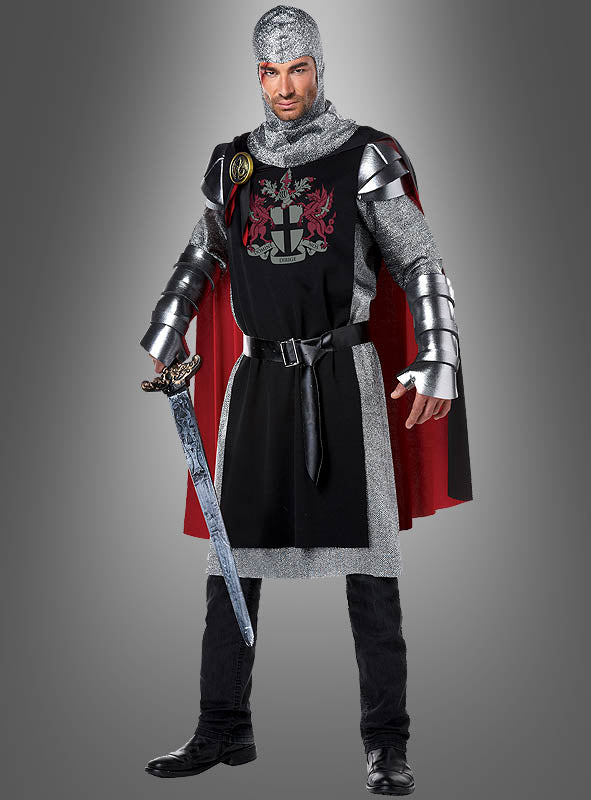 Vor einem schlichten grauen Hintergrund steht ein Mann in einem mittelalterlichen Ritterkostüm mit einem Schwert in der Hand. Er trägt eine schwarze Tunika mit Wappen, silbernes Kettenhemd und einen auffälligen roten Umhang – ein ideales mittelalterliches Ritterkostüm für jeden Anlass.