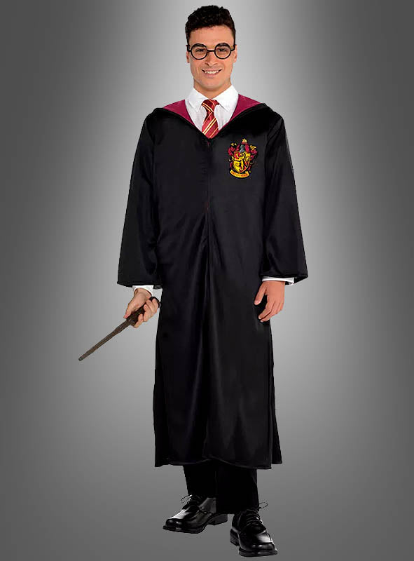 Eine Person, die ein Harry-Potter-Kostüm für Erwachsene mit Zauberstab trägt – bestehend aus einer schwarzen Gryffindor-Robe mit rot-goldenem Wappen, einem weißen Hemd, einer rot gestreiften Krawatte und einer Brille – und einen Zauberstab in der Hand hält, steht vor einem schlichten grauen Hintergrund.