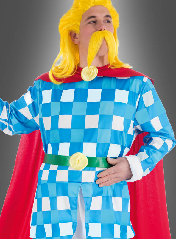 Eine Person, die das „Deluxe Troubadix“-Kostüm aus „Asterix“ trägt – bestehend aus einem blau-weiß karierten Outfit mit rotem Umhang, grünem Gürtel, gelber Perücke und gelbem Schnurrbart –, ein auf den ersten Blick erkennbarer Look, der von der beliebten Comicfigur inspiriert ist, vor einem grauen Hintergrund.