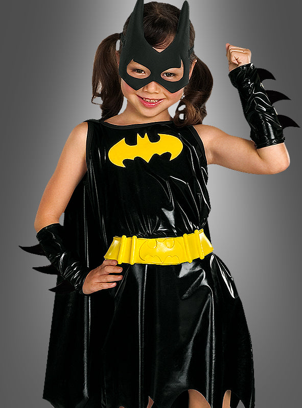 Ein junges Mädchen trägt das „Batgirl Deluxe“-Kinderkostüm, bestehend aus einem schwarzen Anzug mit gelbem Gürtel und Logo, einer passenden Maske und schwarzen Handschuhen, und steht selbstbewusst als Superheldin vor einem schlichten grauen Hintergrund.