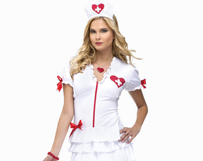 Eine Person in einem weißen Krankenschwesterkostüm mit roten Akzenten, darunter ein Herz mit einem Kreuz, rote Schleifen und eine dazu passende Krankenschwesterhaube, steht vor einem einfarbigen Hintergrund.