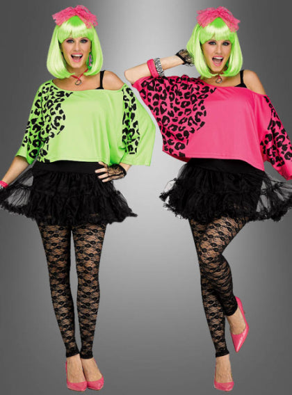 Zwei Frauen tragen neongrüne und pinkfarbene Perücken, dazu passende Oberteile mit Animal-Print, schwarze Tutus, Spitzenleggings und pinkfarbene Ballerinas und posieren fröhlich vor einem grauen Hintergrund.