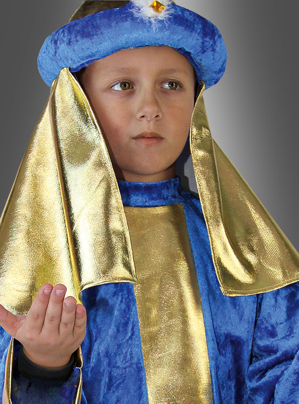 Ein Kind, das das „Weiser aus dem Morgenland – blaues Kinderkostüm“ mit passender Kopfbedeckung trägt, blickt mit erhobener Hand nach vorne und erinnert an eine Figur aus einem Krippenspiel, vor grauem Hintergrund.