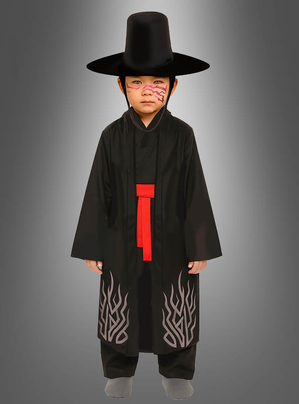 Ein Kind, das das K-Pop-Kostüm „Black Demon“ für Jungen trägt – bestehend aus einem schwarzen, traditionellen Gewand mit grauen Mustern, einem roten Gürtel, einem hohen schwarzen Hut und rosa Gesichtsbemalung –, steht vor einem grauen Hintergrund mit Farbverlauf und bringt so den unverwechselbaren Stil dieses Manga-Cosplays oder Dämonen-Kostüms perfekt zur Geltung.