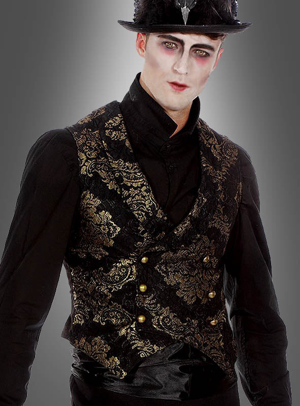 Eine Person, die ein schwarzes Hemd und die „Luxus Gothic Goldbrokat Weste“ – eine aufwendig verzierte schwarz-goldene Weste – trägt, dazu einen schwarzen Hut, blasses Make-up und dunklen Lidschatten, steht vor einem grauen Hintergrund; dieses Ensemble ist von der viktorianischen Mode inspiriert und verbindet klassische Eleganz mit dramatischem Flair.