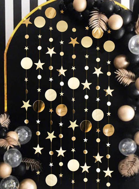 Eine funkelnde Girlande aus goldenen Sternen und Kreisen hängt vor einem schwarzen Hintergrund, ergänzt durch schwarze, goldene und transparente Luftballons sowie metallisch-goldene Blätter – eine elegante, goldene Partydekoration, die bei jeder Feier glänzt.