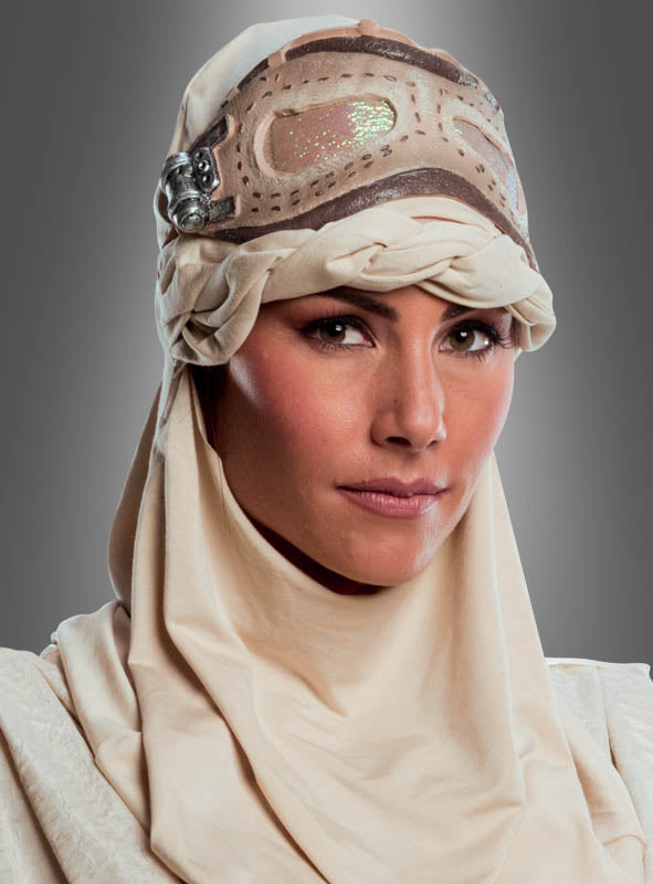 Eine Person, die das „STAR WARS Rey Super Deluxe“-Kostüm trägt, zu dem ein hellbraunes Kopftuch und ein dekorativer Kopfschmuck gehören, blickt mit ausdruckslosem Gesicht vor einem grauen Hintergrund in die Kamera.