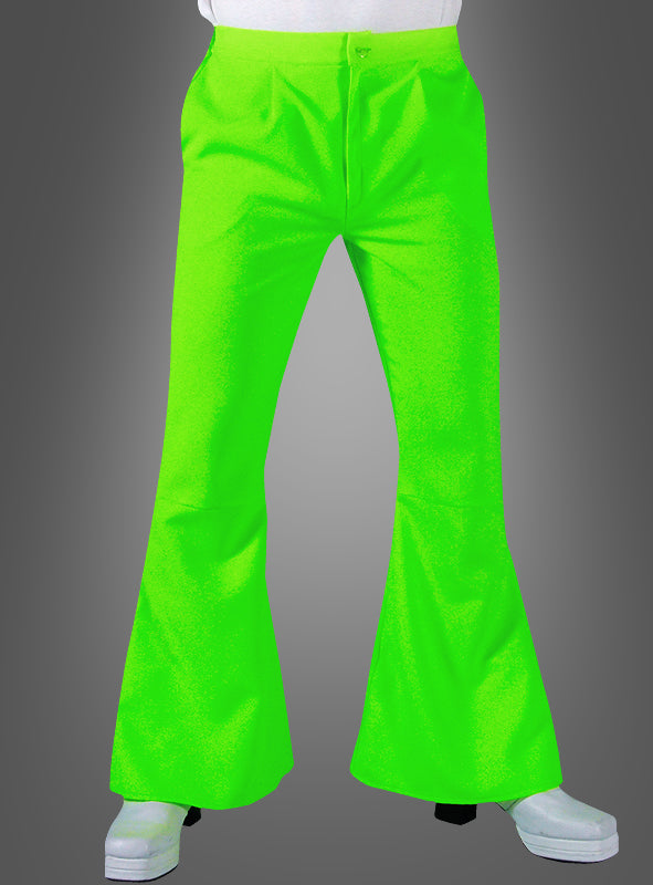 Ein Model trägt eine neongrüne Hippie-Hose mit Schlag für Herren und weiße Schuhe und steht vor einem einfarbigen grauen Hintergrund mit Farbverlauf – ein cooler Look im Retro-Stil.