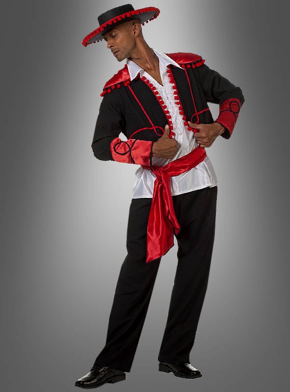 Ein Mann im Flamenco-Tänzer-Kostüm – bestehend aus einer schwarzen Hose, einer schwarzen Jacke mit roten Verzierungen, einem weißen Hemd, einer roten Schärpe und einem schwarzen Hut – posiert vor einem grau verlaufenden Hintergrund.