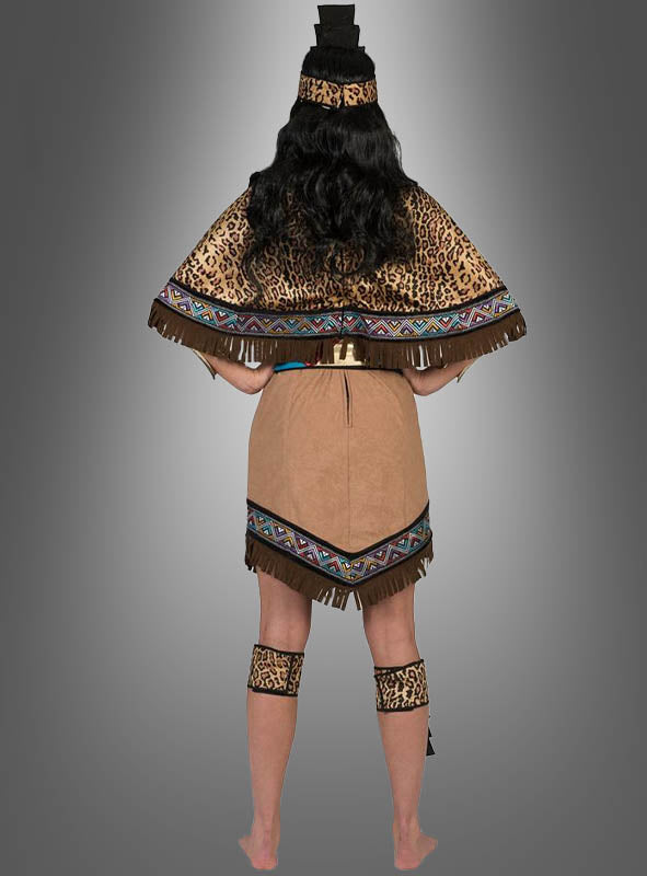 Eine Person steht barfuß und mit dem Rücken zur Kamera und trägt das „Aztekische Königin“-Kostüm – ein hellbraunes Kleid mit Animal-Print-Akzenten, gemusterten Borten und einem passenden Stirnband – vor einem grauen Hintergrund mit Farbverlauf.