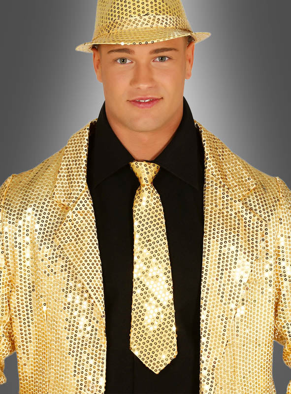 Eine Person steht selbstbewusst vor einem grauen Hintergrund mit Farbverlauf und trägt einen goldenen Paillettenhut sowie eine Jacke mit der schimmernden „Pailletten Krawatten Unisex“ über einem schwarzen Hemd – ein auffälliges Karnevalsaccessoire, das sich perfekt für jede Feier eignet.