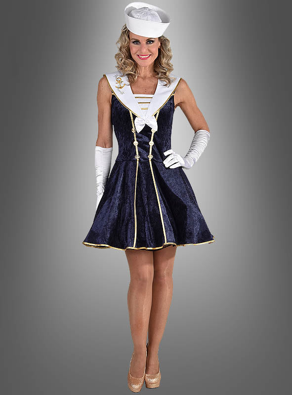 Eine Frau in einem marineblauen Matrosen-Kostümkleid, kombiniert mit einem weißen Hut, Handschuhen und Pumps, steht vor einem neutralen grauen Hintergrund – ideal als zeitloses Karnevalskostüm oder schickes Matrosenkleid für festliche Anlässe.