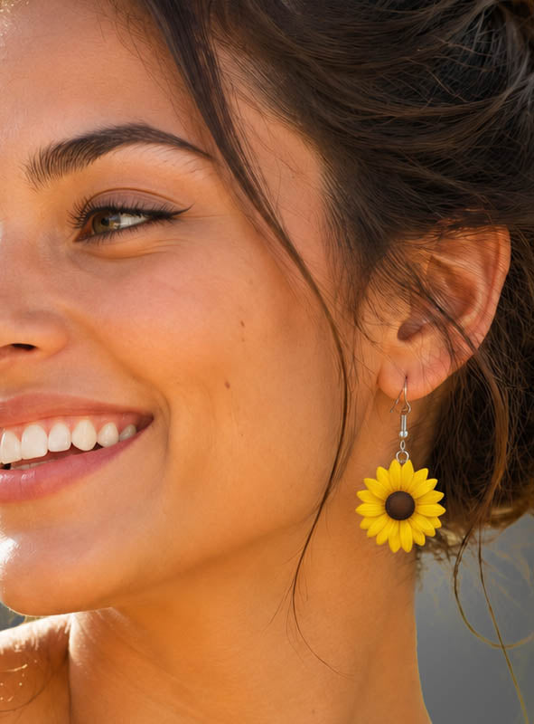 Eine lächelnde Frau mit Flügel-Eyeliner trägt die „Blumen Ohrringe Flower Power“ – große, gelbe Ohrringe in Form von Sonnenblumen, die ihren lebhaften Boho-Look perfekt unterstreichen.