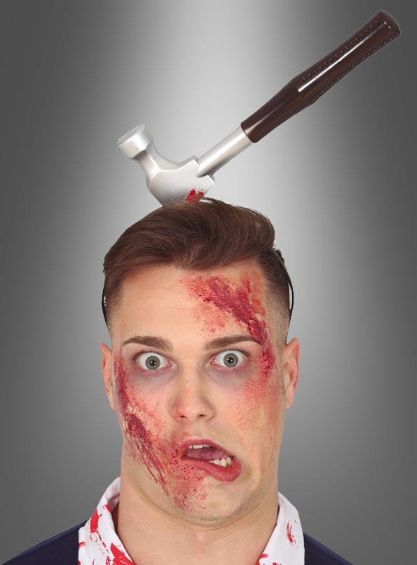 Eine Person mit Kunstblut im Gesicht und dem „Horror Haarreif Werkzeuge im Kopf“ – einem realistisch wirkenden Haarreif in Form eines Hammerkopfs, der scheinbar im Kopf verankert ist – posiert vor einem grauen Hintergrund mit Farbverlauf.