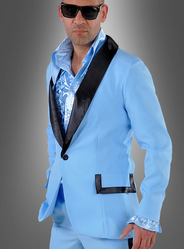 Ein Mann, der einen blauen Anzug aus den 50er Jahren für Herren mit schwarzem Revers, ein glänzendes blaues Hemd und eine Sonnenbrille trägt, steht vor einem grauen Hintergrund mit Farbverlauf und verkörpert damit die Essenz von Vintage-Herrenmode und einen lässigen Rockabilly-Look.
