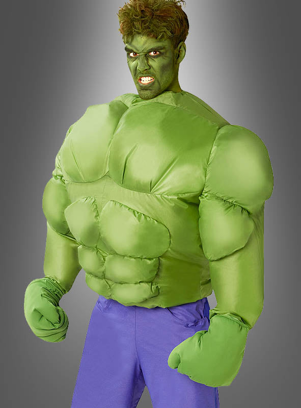 Eine Person trägt das aufblasbare Hulk-Kostüm für Herren mit lila Hose und posiert mit geballten Fäusten wie ein Comic-Superheld vor einem grauen Hintergrund mit Farbverlauf.