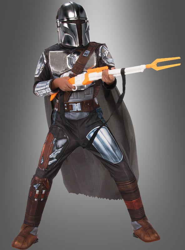 Eine Person trägt das Premium-Mandalorianer-Kinder-Beskar-Kostüm aus „Star Wars“ und steht mit einer Spielzeugwaffe in der Hand da. Die detailreiche Rüstung und der dunkelgraue Umhang sind vor einem schlichten grauen Hintergrund deutlich zu erkennen. Dieses auffällige Kostüm fängt den Geist von „Star Wars“ perfekt ein und ist ideal für jeden jungen Fan.