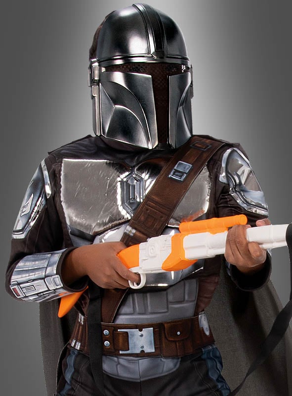 Ein Kind, das das „Premium Mandalorianer Kinder Beskar-Kostüm Star Wars“ trägt, hält vor einem grauen Hintergrund einen Spielzeug-Blaster mit einem orange-weißen Lauf in der Hand.