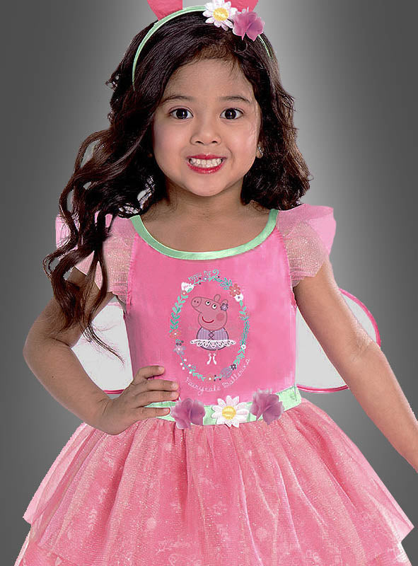 Ein kleines Mädchen trägt das Peppa-Pig-Feenkleid für Mädchen, auf dessen Vorderseite eine niedliche Zeichentrickfigur abgebildet ist, dazu ein geblümtes Stirnband und Feenflügel. Sie steht vor einem schlichten grauen Hintergrund. Dieses bezaubernde Kinderkostüm ist ideal für kleine Peppa-Wutz-Fans.