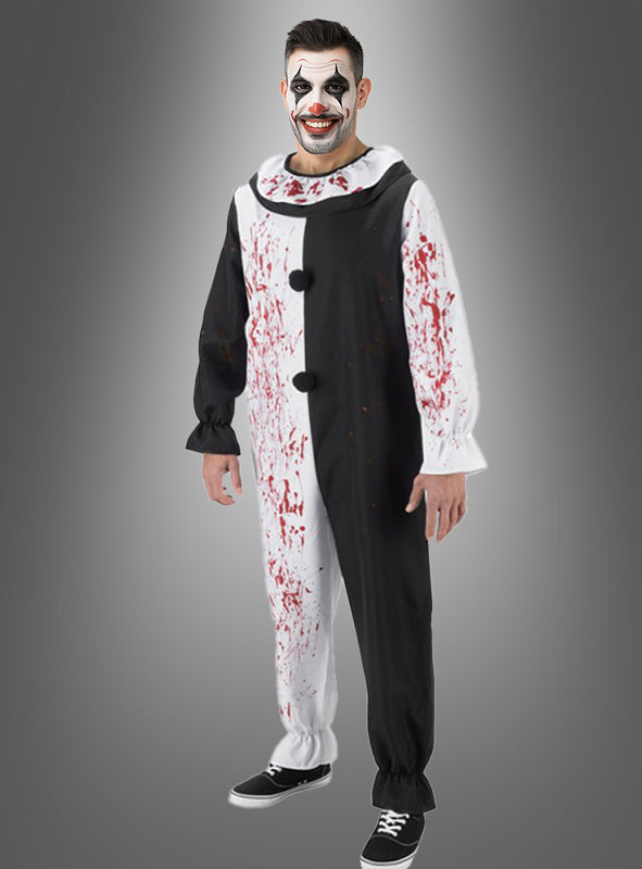 Eine Person im „Terrifier“-Kostüm als Horrorclown „Art the Clown“ – ein schwarz-weißes Clownkostüm mit Blutflecken und passender Gesichtsbemalung –, die vor einem grauen Hintergrund steht und lächelt und dabei die gruselige Ausstrahlung von „Art the Clown“ aus „Terrifier“ einfängt; perfekt für jeden Fan von Horrorclowns.