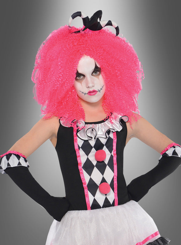Eine Person, die das „Pinky Clown Harlekin“-Kinderkostüm trägt – bestehend aus einem schwarz-weißen Harlekin-Muster mit rosa Besatz, einer großen rosa Lockenperücke, weißes Gesichts-Make-up und schwarzen Lippenstift – steht mit den Händen in die Hüften gestemmt vor einem grauen Hintergrund mit Farbverlauf und ist damit die perfekte Wahl für jede Zirkus-Mottoparty oder als auffälliges Karnevalskostüm.