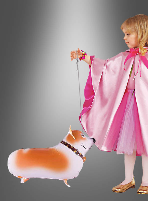 Ein kleines Kind in einem rosa Kostüm hält vor einem grauen Farbverlaufshintergrund eine Leine, an der ein „Hunde Airwalker“-Folienballon in Form eines Corgis befestigt ist.