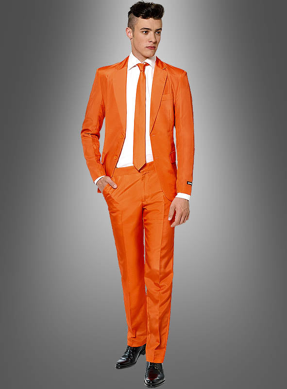 Ein Mann steht vor einem grau abgestuften Hintergrund und trägt den Herrenanzug „Orange Suitmeister“ mit passender Krawatte, weißem Hemd und schwarzen Anzugschuhen – ein wahrhaft eleganter Herrenanzug-Look.