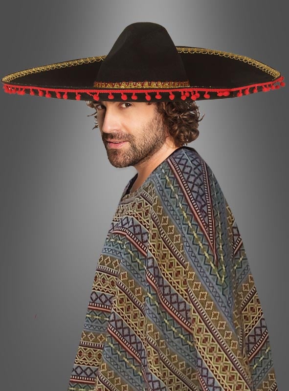 Ein Mann, der einen gemusterten Poncho und einen großen schwarzen Sombrero „Hut XXL Mexikaner“ (ca. 55 cm Umfang) mit roter und goldener Verzierung trägt und vor einem neutralen grauen Hintergrund steht.