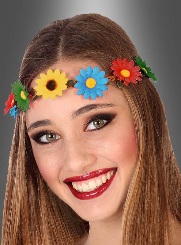 Eine junge Frau mit langen braunen Haaren lächelt vor einem grauen Hintergrund mit Farbverlauf und trägt dabei das von der Flower-Power-Party inspirierte Stirnband mit bunten Blumen.