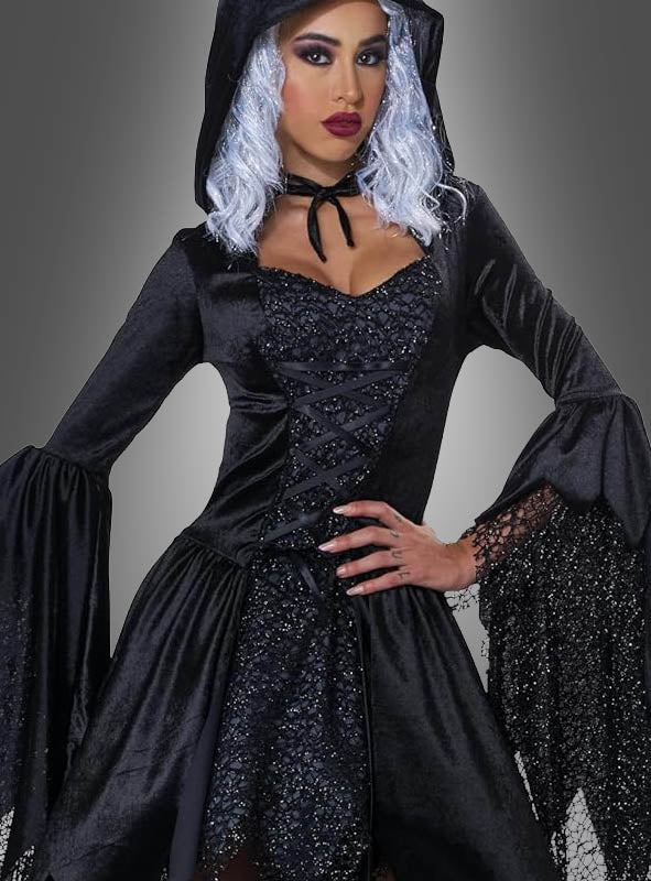 Eine Person, die das „Schwarze Glamour-Hexe-Kleid mit Kapuze“ trägt – ein schwarzes Kleid mit Kapuze, ausgestellten Ärmeln und zarten Spitzendetails –, posiert elegant vor einem grauen Hintergrund.