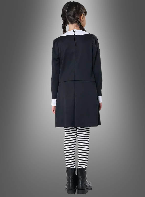 Ein Mädchen mit geflochtenen Zöpfen, das das „Dunkles Gothic Mädchen“-Kostüm trägt – bestehend aus einem schwarzen Kleid, einer Bluse mit weißem Kragen, schwarzen Stiefeln und schwarz-weiß gestreiften Leggings –, steht mit dem Rücken zur Kamera vor einem grauen Hintergrund.