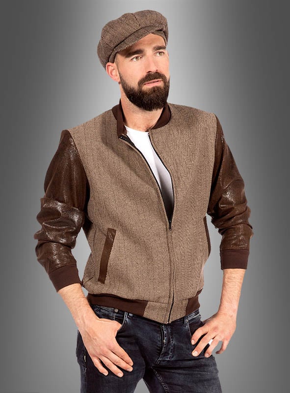 Ein bärtiger Mann trägt eine braune Schirmmütze, die Vintage-Herrenjacke „Duke Rockabilly“ in Braun und Beige, ein weißes T-Shirt und Jeans und steht mit den Händen in den Taschen vor einem grauen Hintergrund mit Farbverlauf.